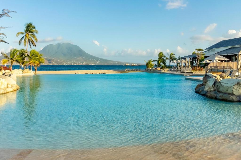 einen Pool neben einem Strand mit Palmen in der Unterkunft Park Hyatt St. Kitts in Christophe Harbour