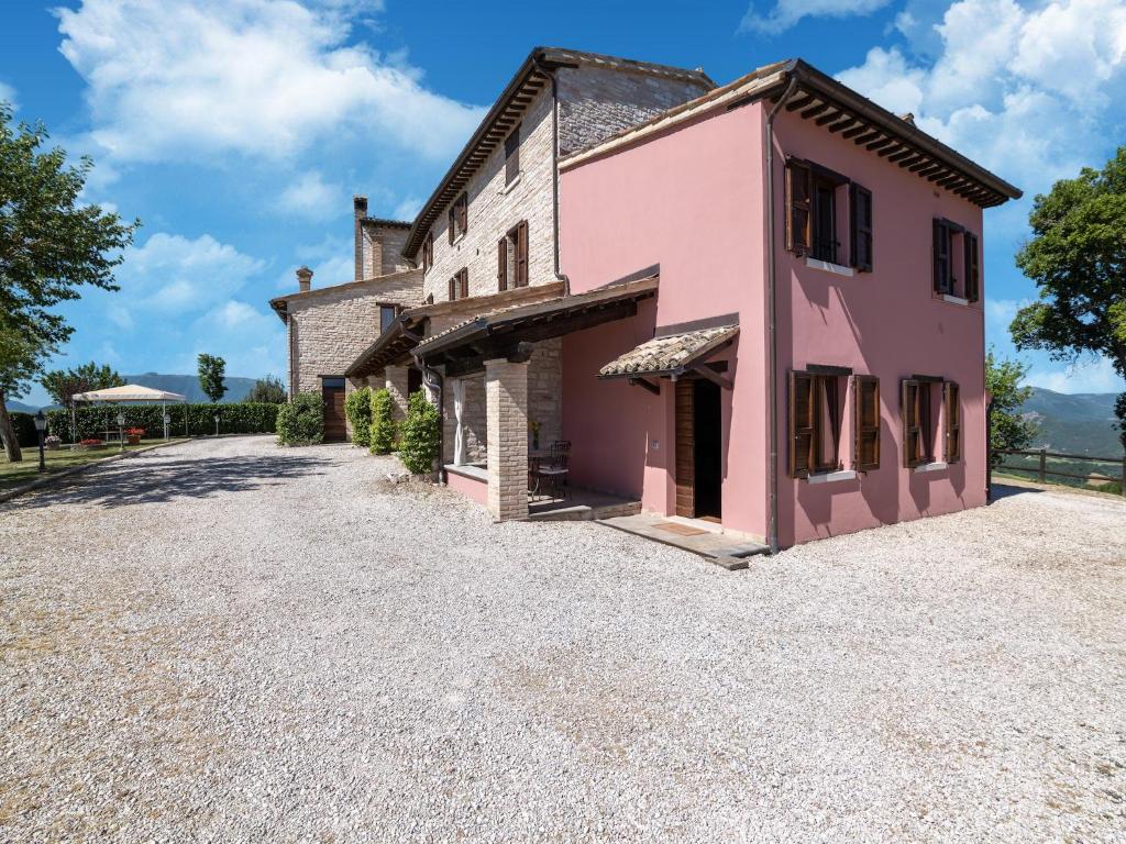 an old pink house with a gravel driveway at Apartment in a farmhouse with 2 swimming pools in Cagli