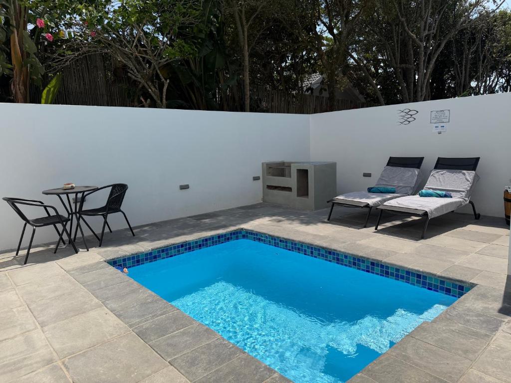 einen Pool mit einem Tisch und Stühlen neben einer weißen Wand in der Unterkunft Ocean Whisper in Plettenberg Bay