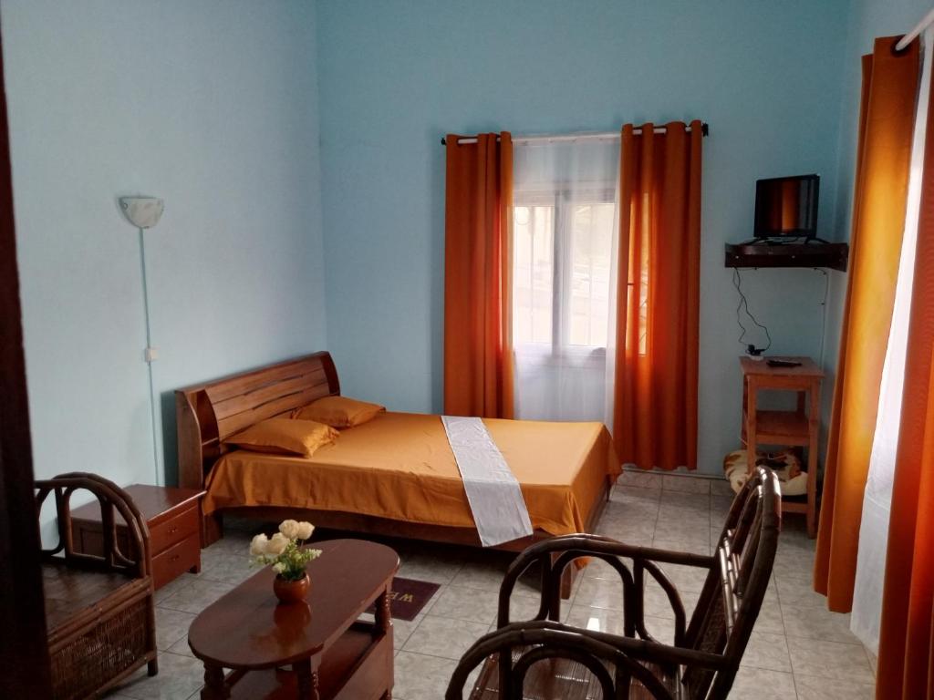 ein Schlafzimmer mit einem Bett mit orangefarbenen Vorhängen und einem Tisch in der Unterkunft Ami Hotel in Fianarantsoa