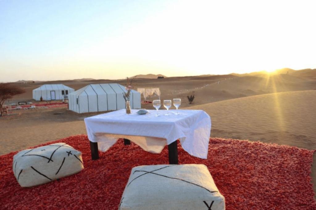 een tafel midden in de woestijn met wijnglazen bij Chegaga Infinite Dunes Luxury Desert Camp in Mhamid