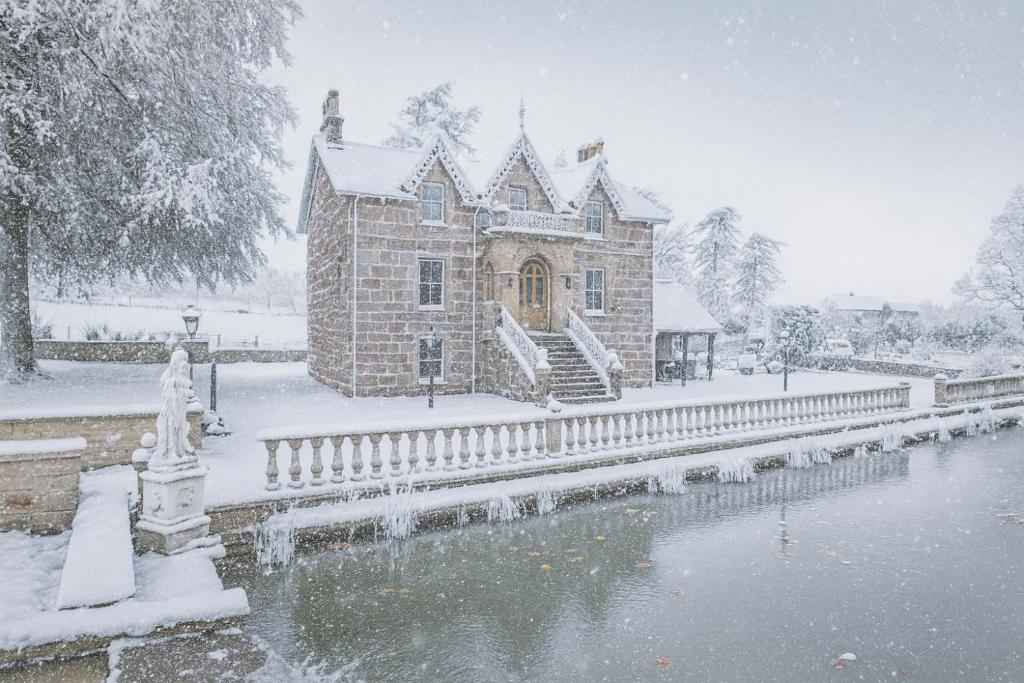 a building covered in snow next to a body of water at The Doune, Luxury Traditional Country House with hot tub in Inverness