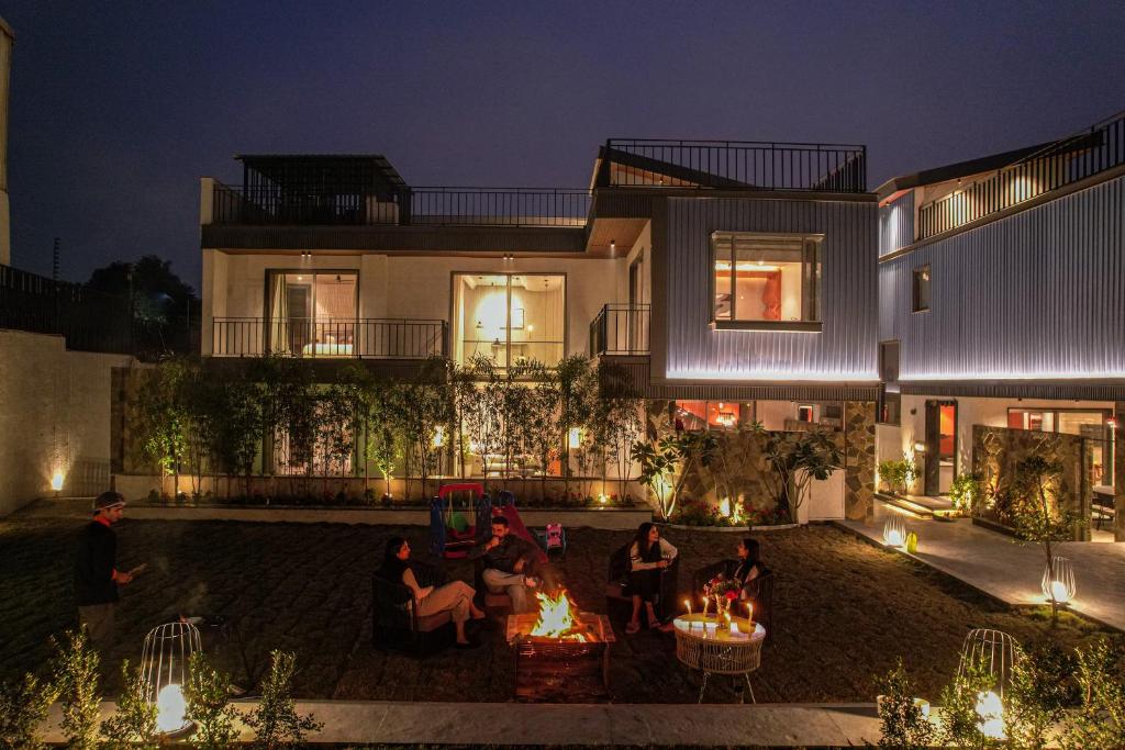 a group of people sitting around a fire in front of a house at SaffronStays Boudhi Tree Villas in Rishīkesh