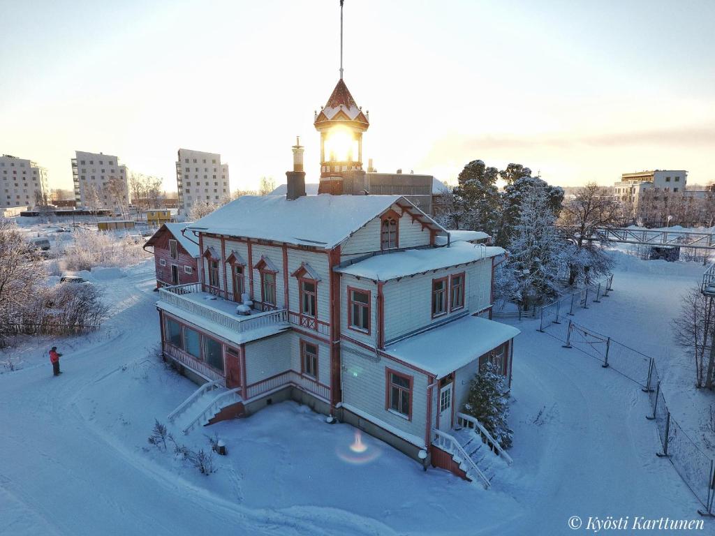 een huis met een toren erop in de sneeuw bij Hostel Cafe Huvila in Oulu