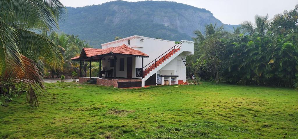 a small house in a field with a mountain in the background at LBS Farmstay in Alāndurai