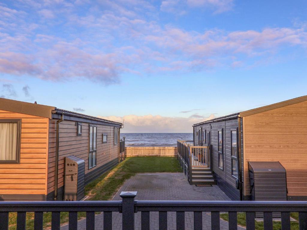 two houses on the beach with the ocean in the background at Paws By The Sea in Norwich