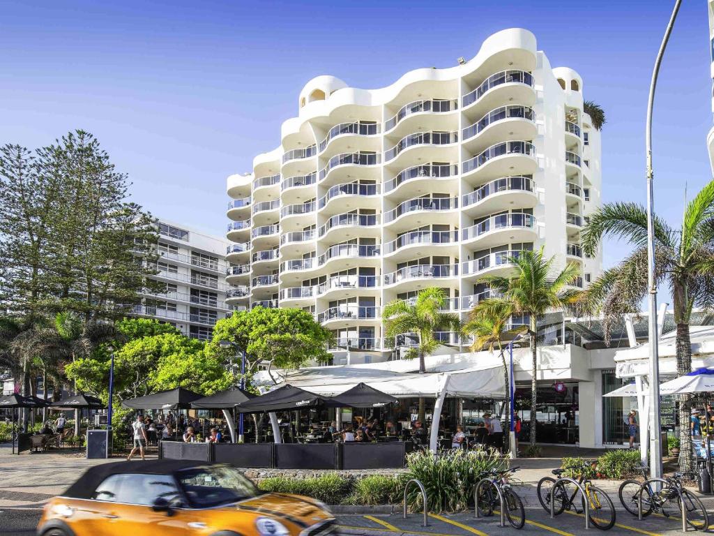 een oranje auto geparkeerd voor een groot gebouw bij Mantra Zanzibar in Mooloolaba