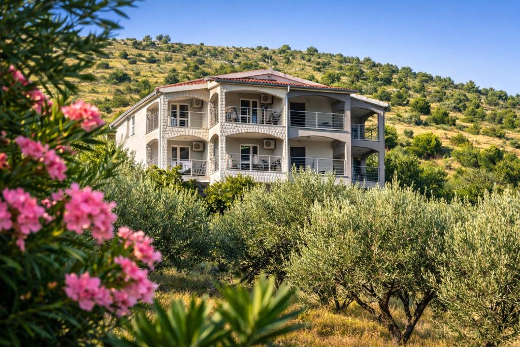 een groot wit huis op een heuvel met roze bloemen bij Apartments VillaMare in Grebaštica