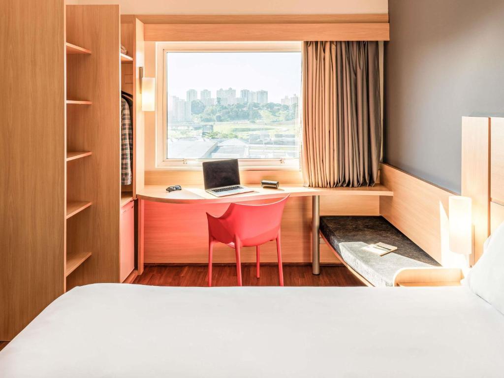 a hotel room with a bed and a desk with a laptop at ibis Sao Jose dos Campos Dutra in São José dos Campos