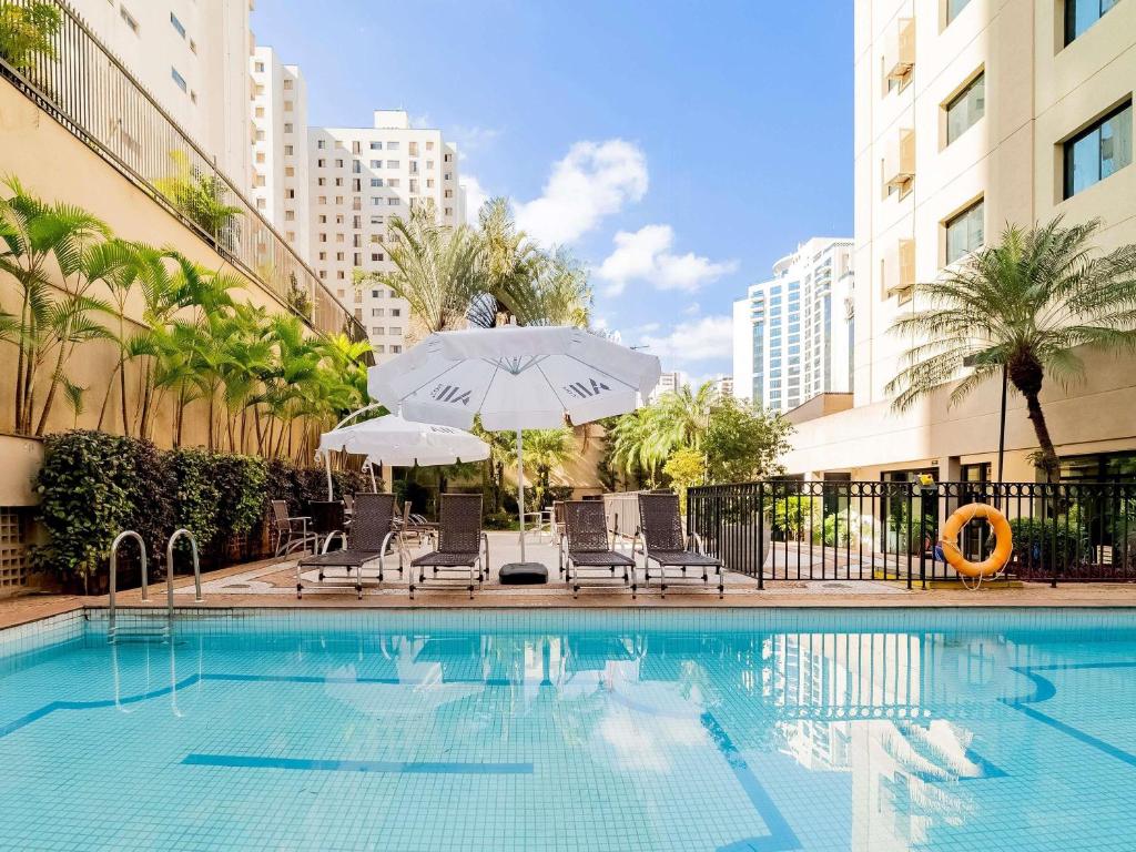 een zwembad met stoelen en parasols naast een gebouw bij Mercure São Paulo Ibirapuera Privilege in Sao Paulo