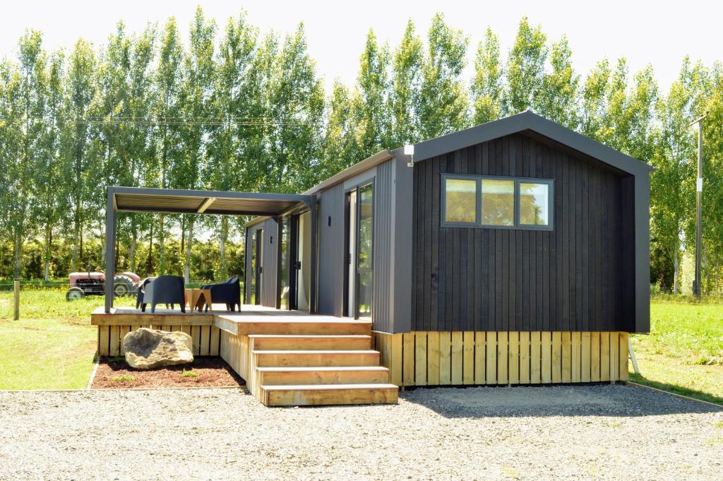 a black tiny house with a porch and stairs at Tihi in Otorohanga