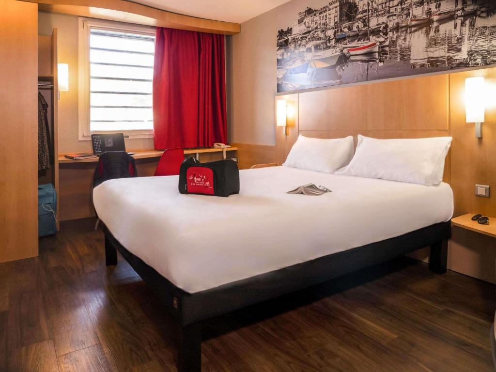 una camera d'albergo con un grande letto con una borsa sopra di ibis Cannes Mandelieu a Mandelieu La Napoule