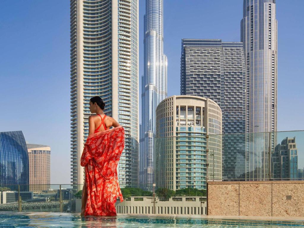 Eine Frau in einem roten Kleid steht im Wasser in einer Stadt in der Unterkunft Sofitel Dubai Downtown in Dubai