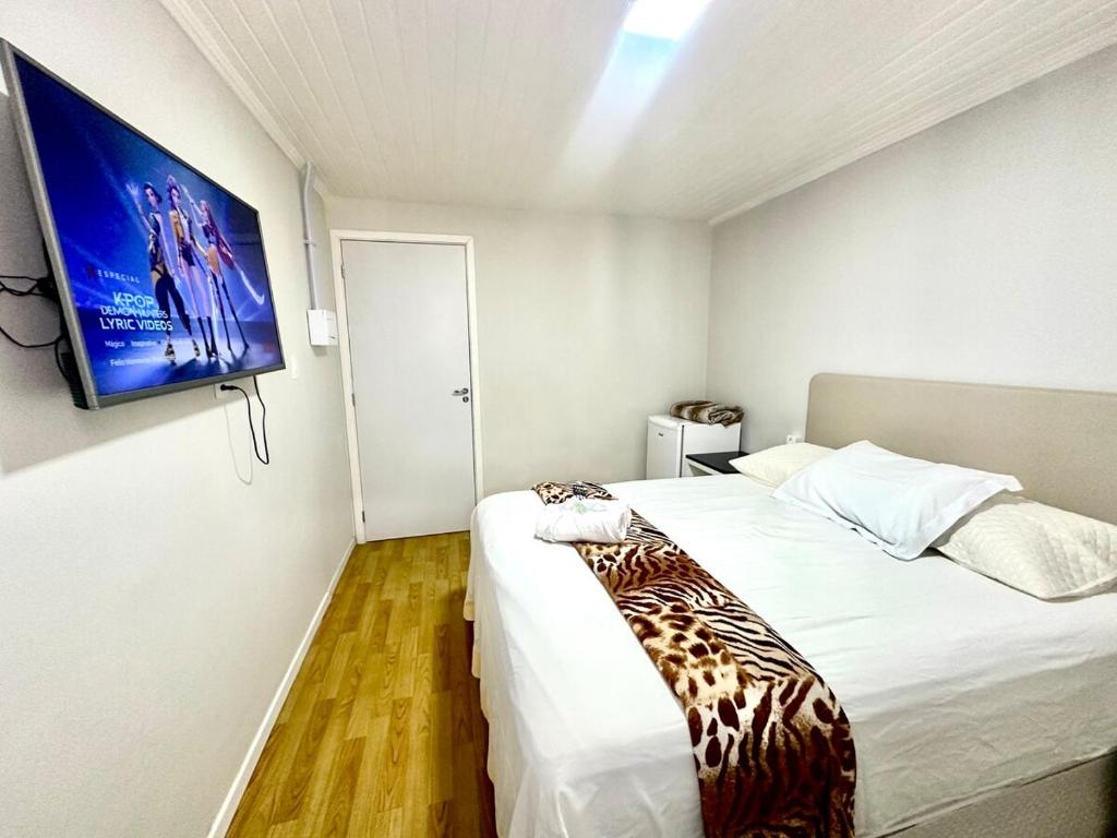 a bedroom with a bed with a television on the wall at Suíte Quarto 3km de Florianópolis in São José