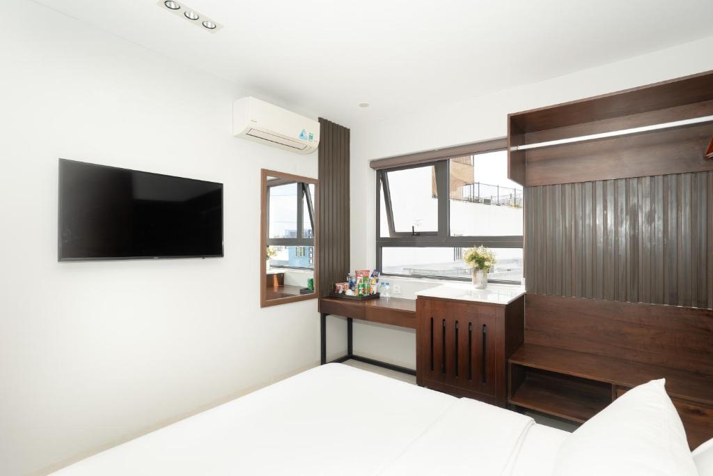 A compact bright bedroom with a wall-mounted TV, desk, window and built-in wood storage.