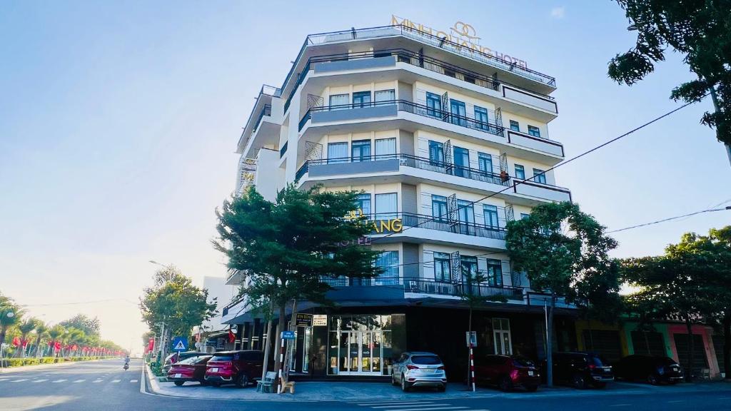 a tall white building with cars parked in front of it at Khách sạn Minh Quang in Phan Rang