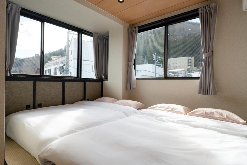 due letti in una stanza con ampie finestre di AURA YUZAWA Apartment Hotel - 1Bedroom Apartment with Living Dining Kitchen Sleeps 2 to 4, Bedroom with 2-Double Bed, Living Room with 1-Sofa Bed a Yuzawa