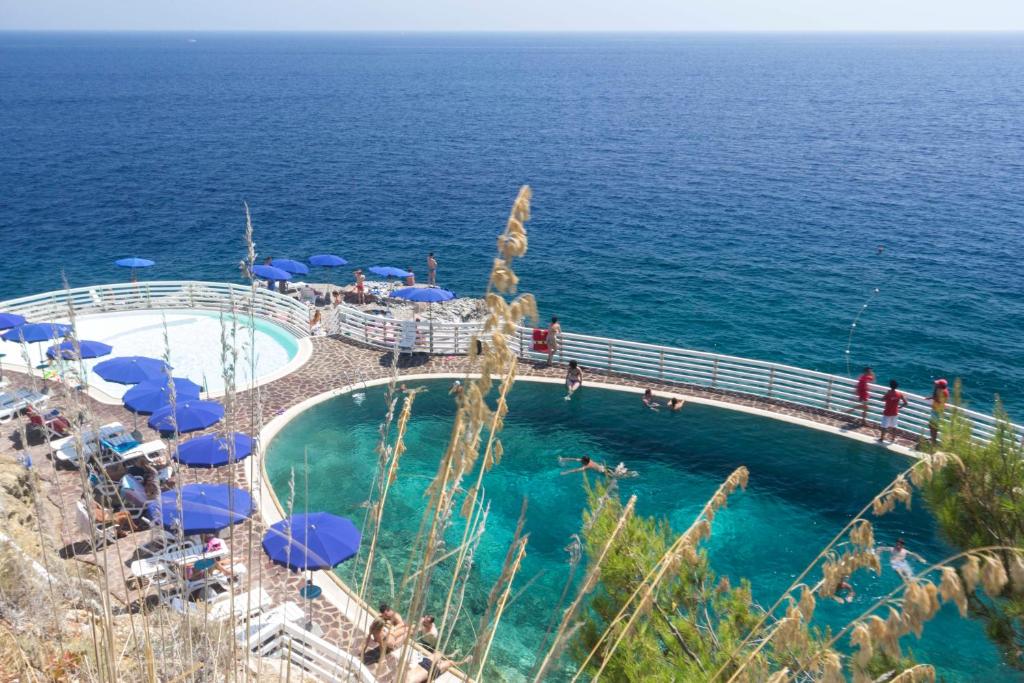 a swimming pool with blue umbrellas and the ocean at Capo d'Arco - Goelba in Rio Marina