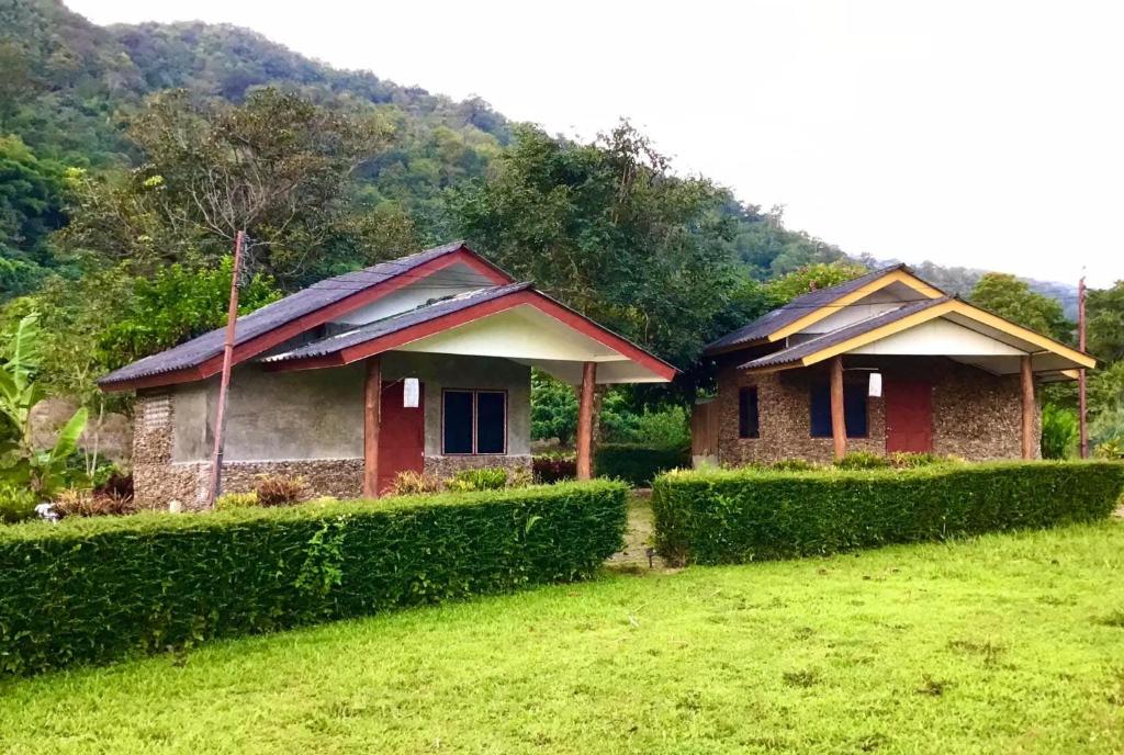 two houses in a field next to a hedge at Doi Lom Elephant farmstay in Ban Muang Kut