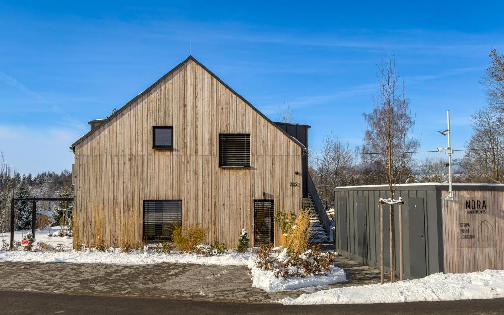 a large wooden barn in the snow with a fence at Nora Apartments in Dolní Morava