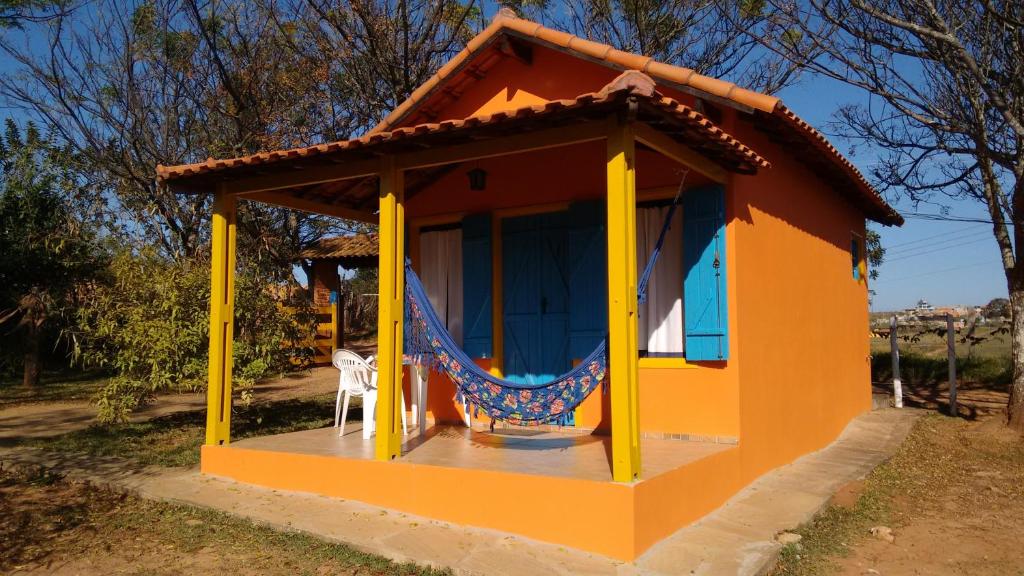 una pequeña casa amarilla y naranja con una silla. en Pousada Recanto do Sossego en São Thomé das Letras