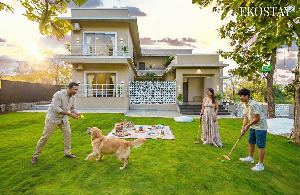 a group of people playing with a dog in front of a house at EKOSTAY - Alpine Villa in Alibaug