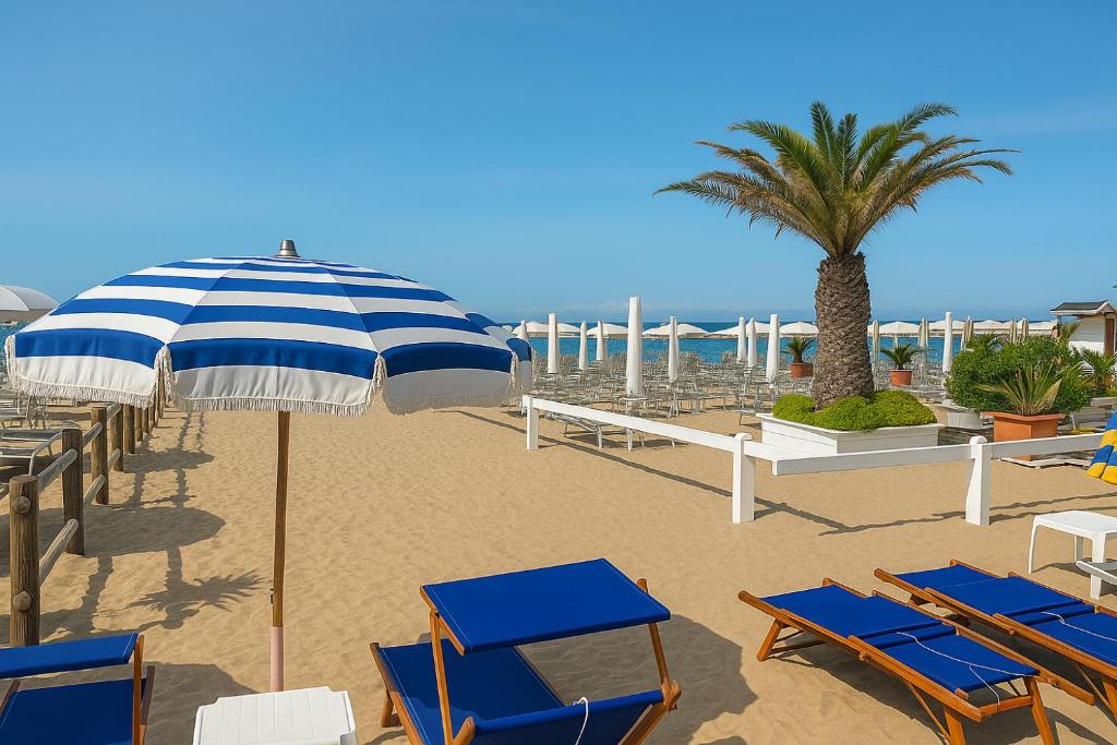a beach with chairs and an umbrella and a palm tree at Villa Chiara in Follonica