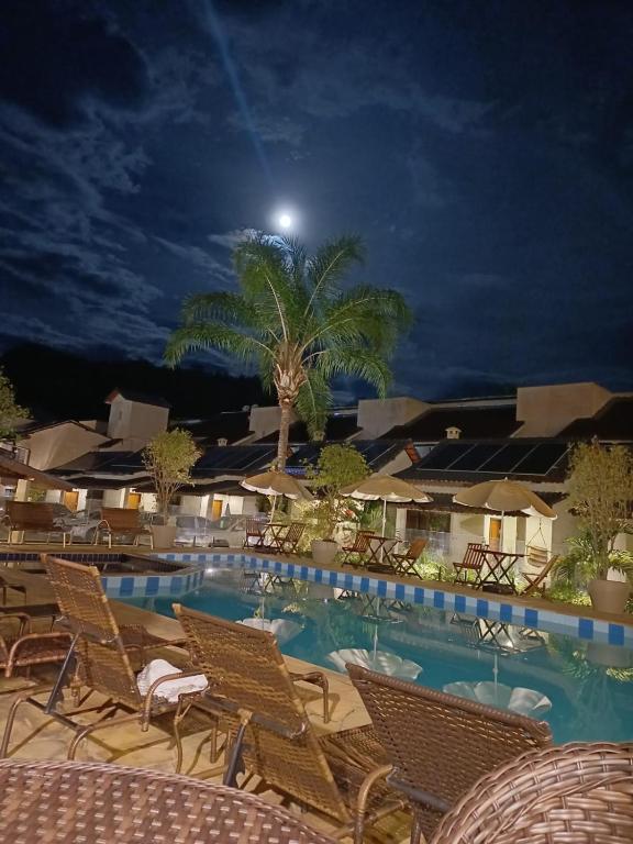 a swimming pool at night with chairs and a palm tree at Pousada do Sol in Penedo
