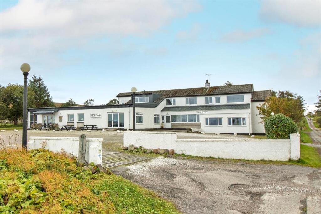 a large white house with a driveway in front of it at Ocean View Bar & Rooms in Laide