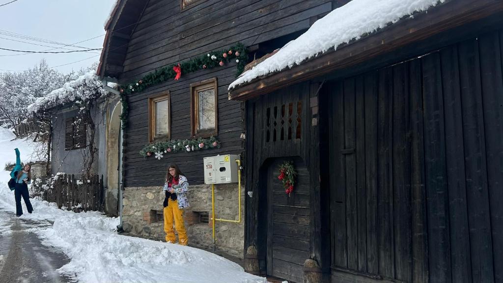 a woman standing outside of a house in the snow at Casa veche “Old house” in Sibiel