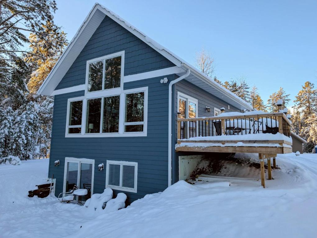 a blue house with a deck in the snow at Driftwood Cabin near Eagle River, WI in Saint Germain