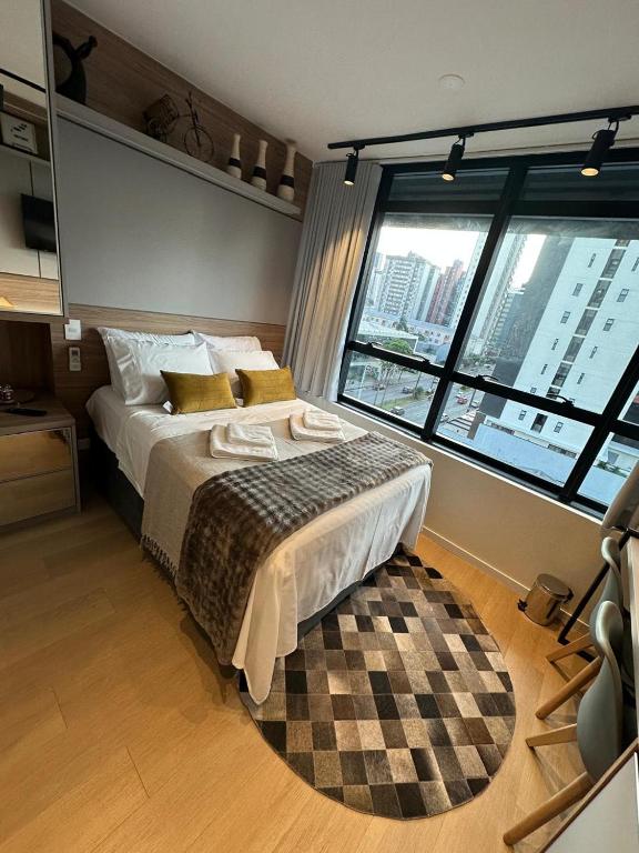 a bedroom with a large bed and a large window at Studio perto Shopping Estação com Piscina interna aquecida, Academia e Terraço Lindo pôr do Sol in Curitiba