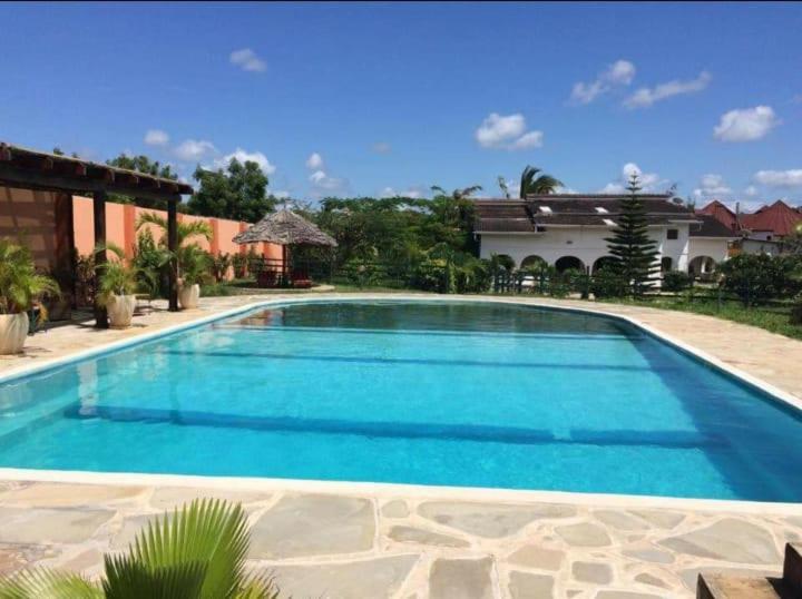 a large blue swimming pool in front of a house at Diani Tembo One Bedroom in Mombasa