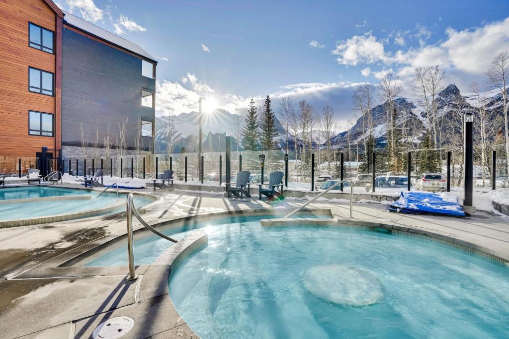 een jacuzzi voor een gebouw met besneeuwde bergen op de achtergrond bij 3 Bedroom with Heated Outdoor Pool and Hottub! in Canmore