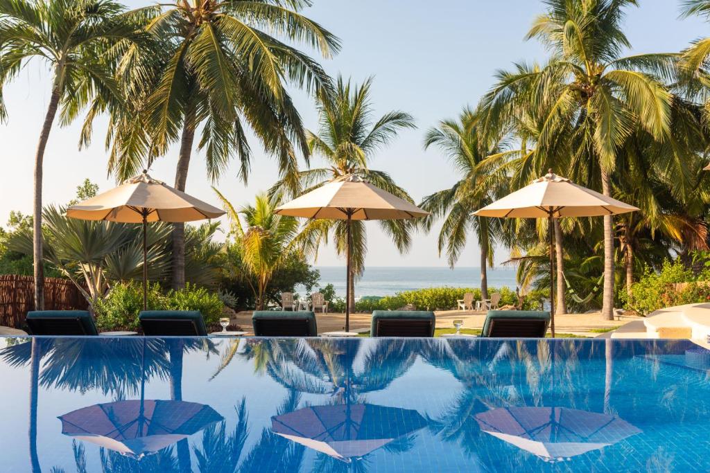 a swimming pool with umbrellas and the ocean at Casa de la Costa in Troncones