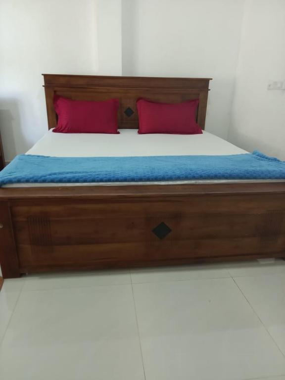 a bed with a wooden frame and red pillows on it at Bosadi Homestay in Katunayaka