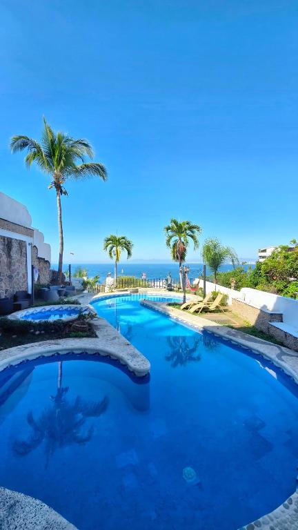 a large swimming pool with palm trees and the ocean at Hillside Villa with ocean views in Puerto Vallarta