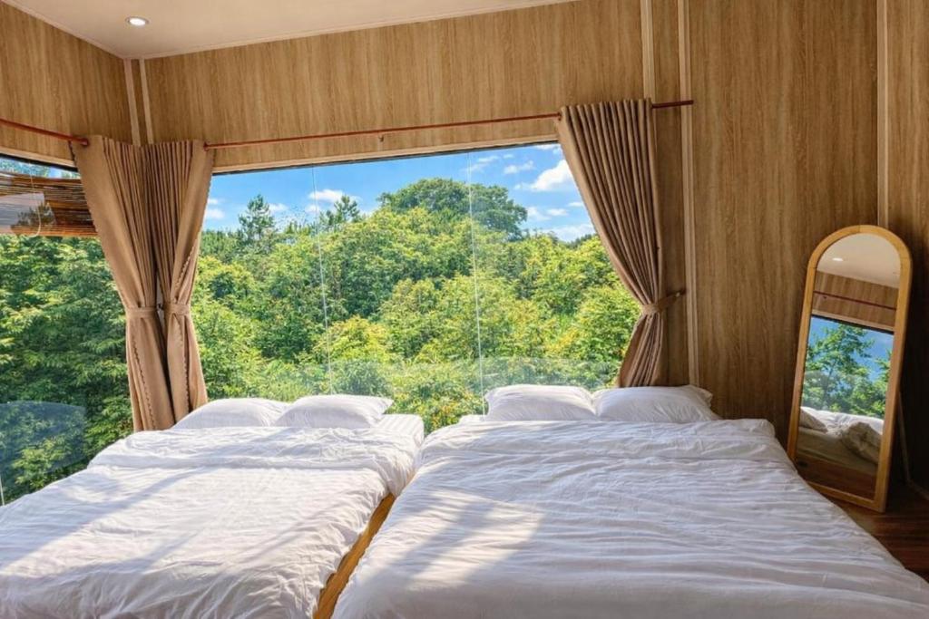 twee bedden in een kamer met een groot raam bij Han San Homestay Măng Đen in Kon Plong