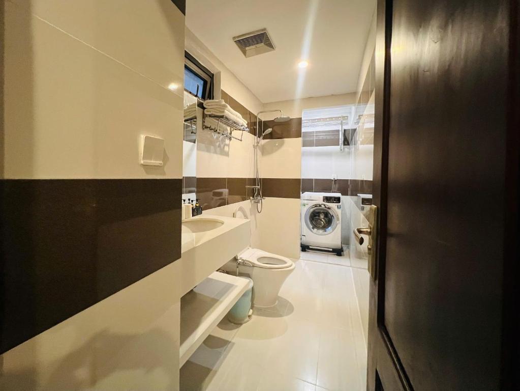 A narrow bathroom with a toilet, wall-mounted sink, shower and washing machine.