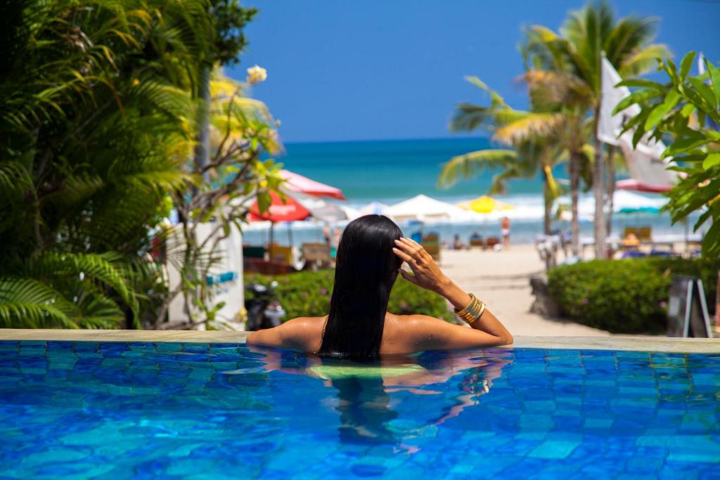 a woman sitting in a swimming pool next to the beach at Away Bali Legian Camakila Resort in Legian