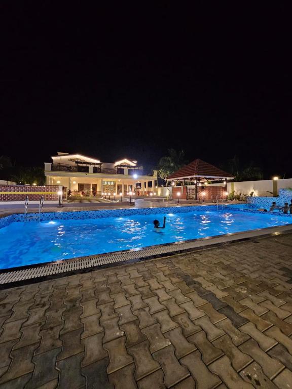 Ein Schwimmbad bei Nacht mit einem Gebäude im Hintergrund in der Unterkunft Kurunchi Malar Resorts in Hosur