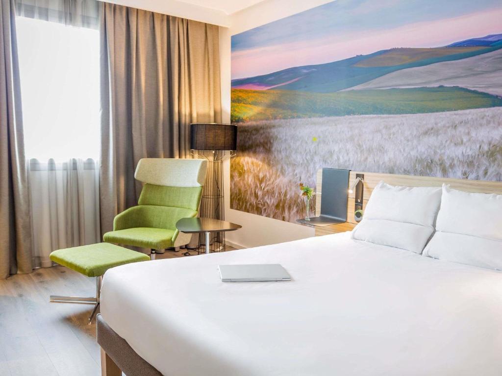een hotelkamer met een bed en een groene stoel bij Novotel Sevilla in Sevilla
