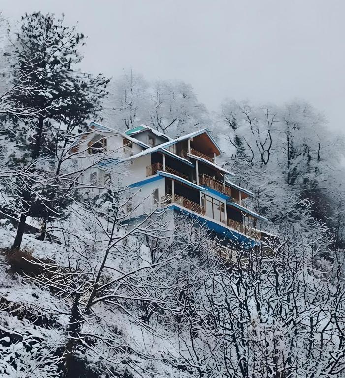 a building on a snowy hill with snow covered trees at Maverick HomeStay in Baragrān