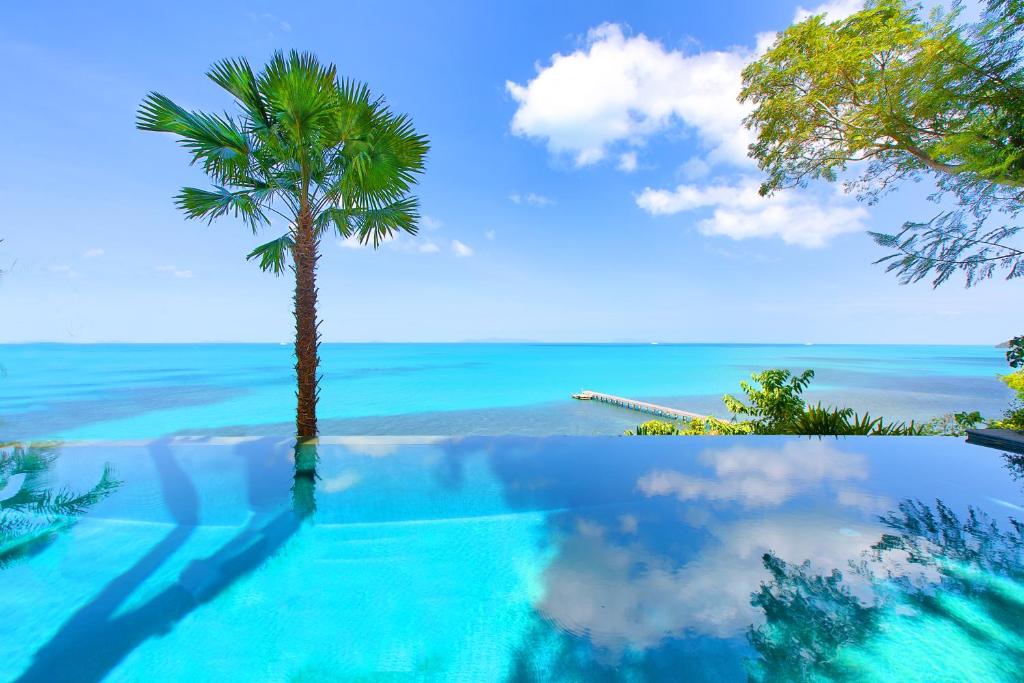 a swimming pool with a palm tree and the ocean at The Headland Villa 2, Samui in Koh Samui