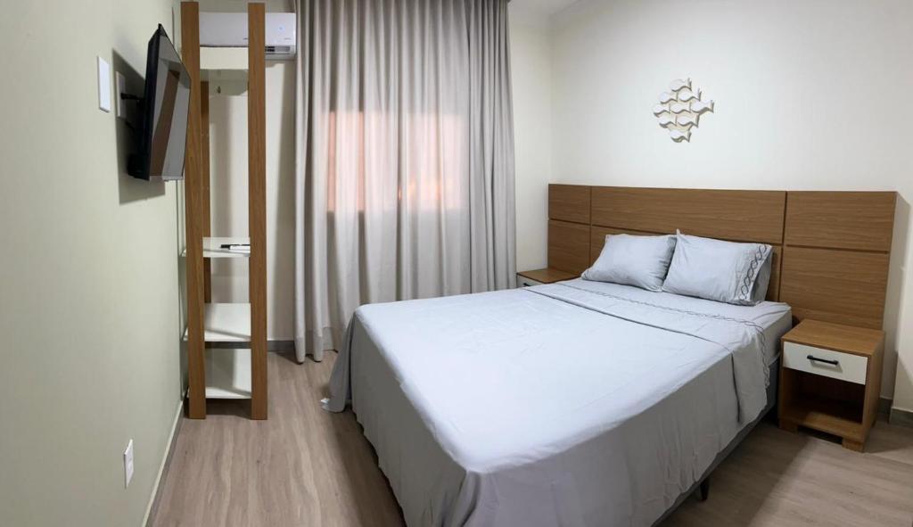 a bedroom with a white bed and a television at quarto standart 2 pousada village in Guarapari