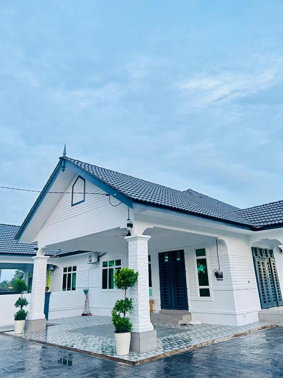 a white house with two potted plants in front of it at Alaisya Homestay in Kampung Raja