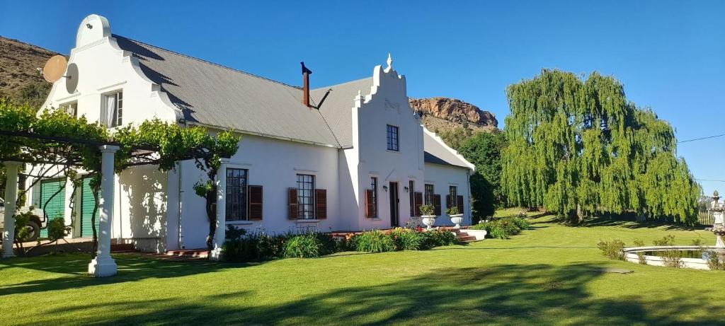 a white house with a green yard and trees at De Kleine Kaap Guesthouse in Lady Grey