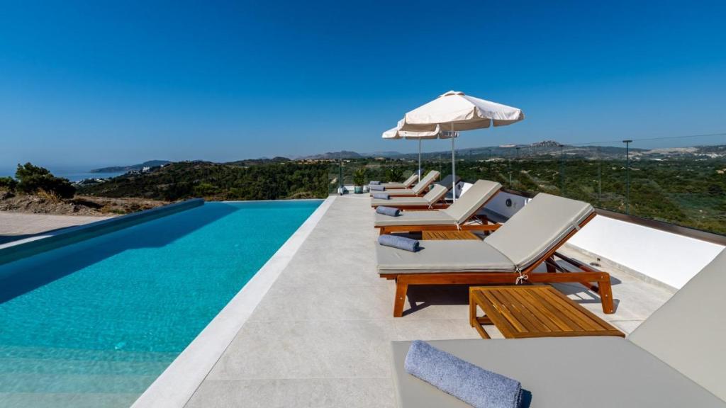 a villa with a swimming pool with chairs and an umbrella at Agnanti Sea View Villa in Koskinou