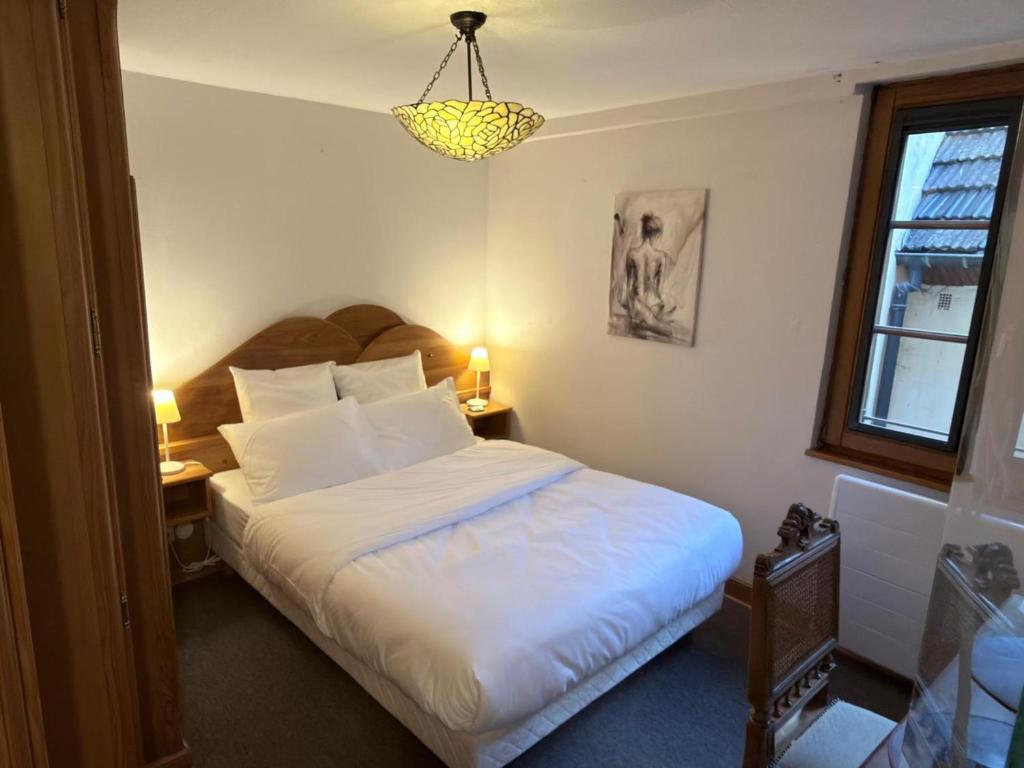 a bedroom with a bed with white sheets and a chandelier at Hôtel Le Sarment d'Or in Riquewihr
