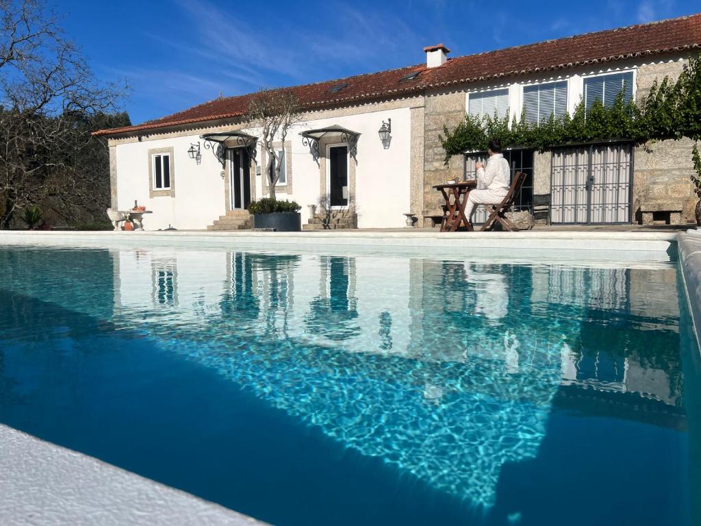 a man sitting in front of a house with a swimming pool at Casa de Rompecias in Vizela